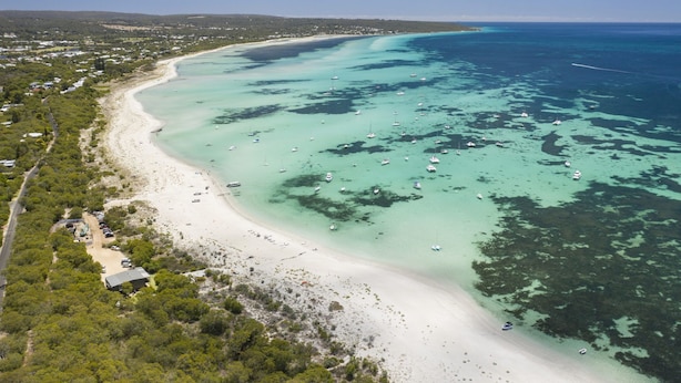Eine Luftaufnahme einer Küstenlandschaft mit Sandstrand, klarem türkisblauem Wasser und vereinzelten Booten.