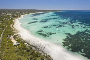 An aerial view of a coastal area with a sandy beach, clear turquoise waters, and scattered boats.