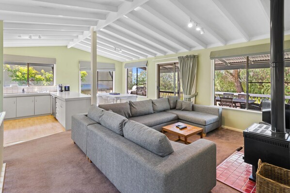 A spacious living area with a grey sectional sofa, a wooden coffee table, and a black wood stove. - Pet Friendly, Fuss Free Quindalup Beach House (Quindalup)