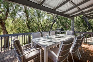 A covered outdoor patio with a table and chairs, surrounded by trees.