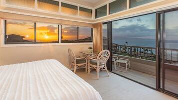 Une chambre d’hôtel avec un grand lit, un balcon doté d’une table et de chaises, et une vue imprenable sur le coucher de soleil.