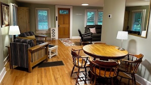 A dining area with a wooden table and chairs, a sofa, and a lamp. - Rivers Edge Cabin, Swimming, Tubing, Fishing, Fire Pit, Grill, Wi-Fi, Relaxing! (Burnsville)