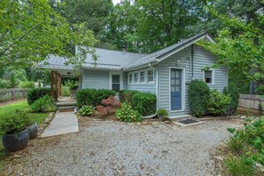 A single-story house with a front porch, a gravel driveway, and a variety of shrubs and plants around the property. - Cabin on the River+Fire Pit+Grill, WiFi, Private! (Burnsville)