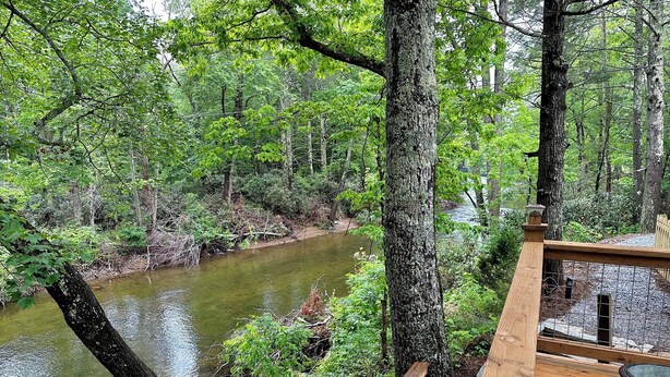 A wooden deck overlooking a river with dense forest. - Rivers Edge Cabin, Swimming, Tubing, Fishing, Fire Pit, Grill, Wi-Fi, Relaxing! (Burnsville)
