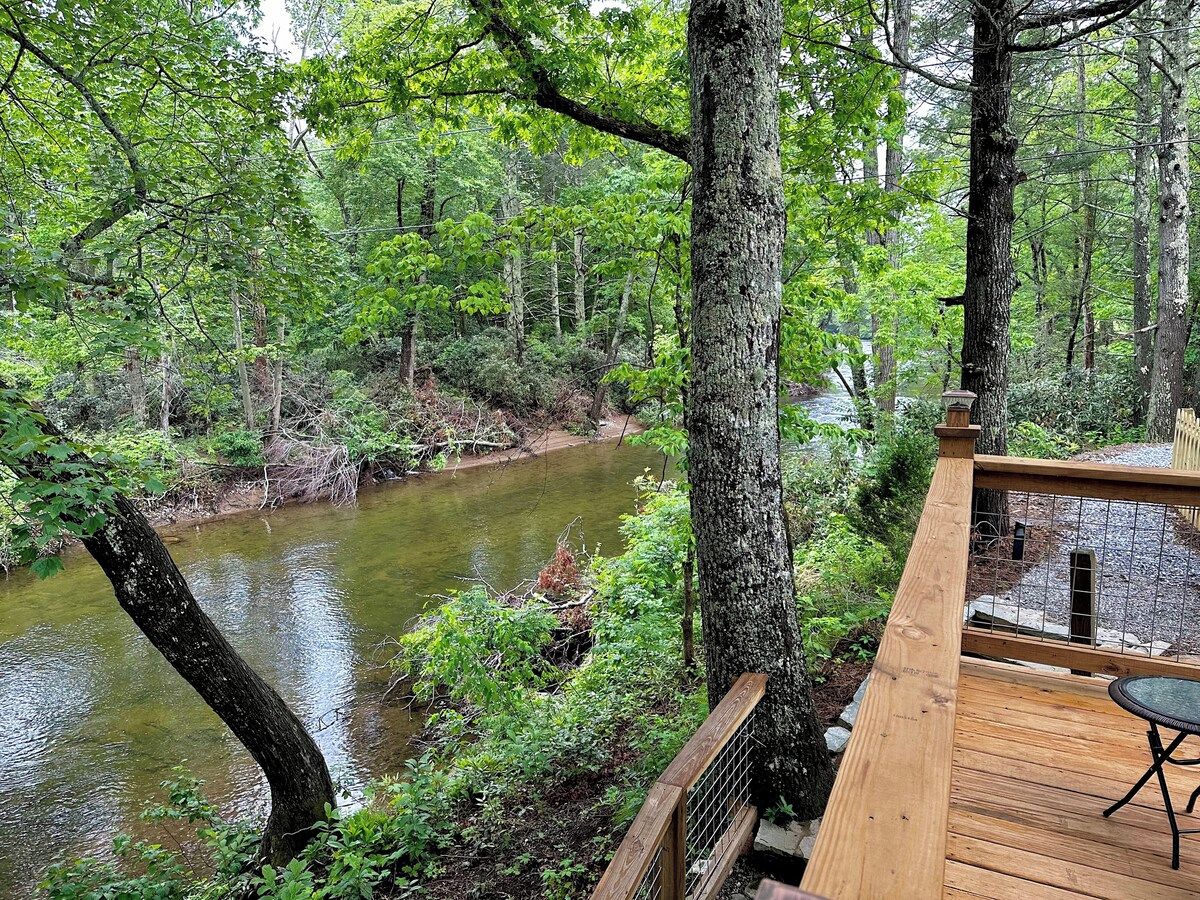 Een houten terras met uitzicht op een rivier, omringd door dicht bos.