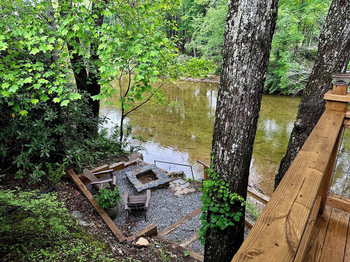 A wooden deck overlooking a pond with a fire pit and seating area.