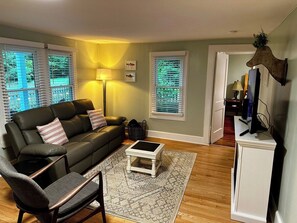 A living room with a sofa, armchair, coffee table, and a television on a stand.