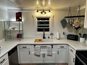 A kitchen with white cabinetry, a countertop, a sink, a window, and hanging pots. - Cabin on the River+Fire Pit+Grill, WiFi, Private! (Burnsville)