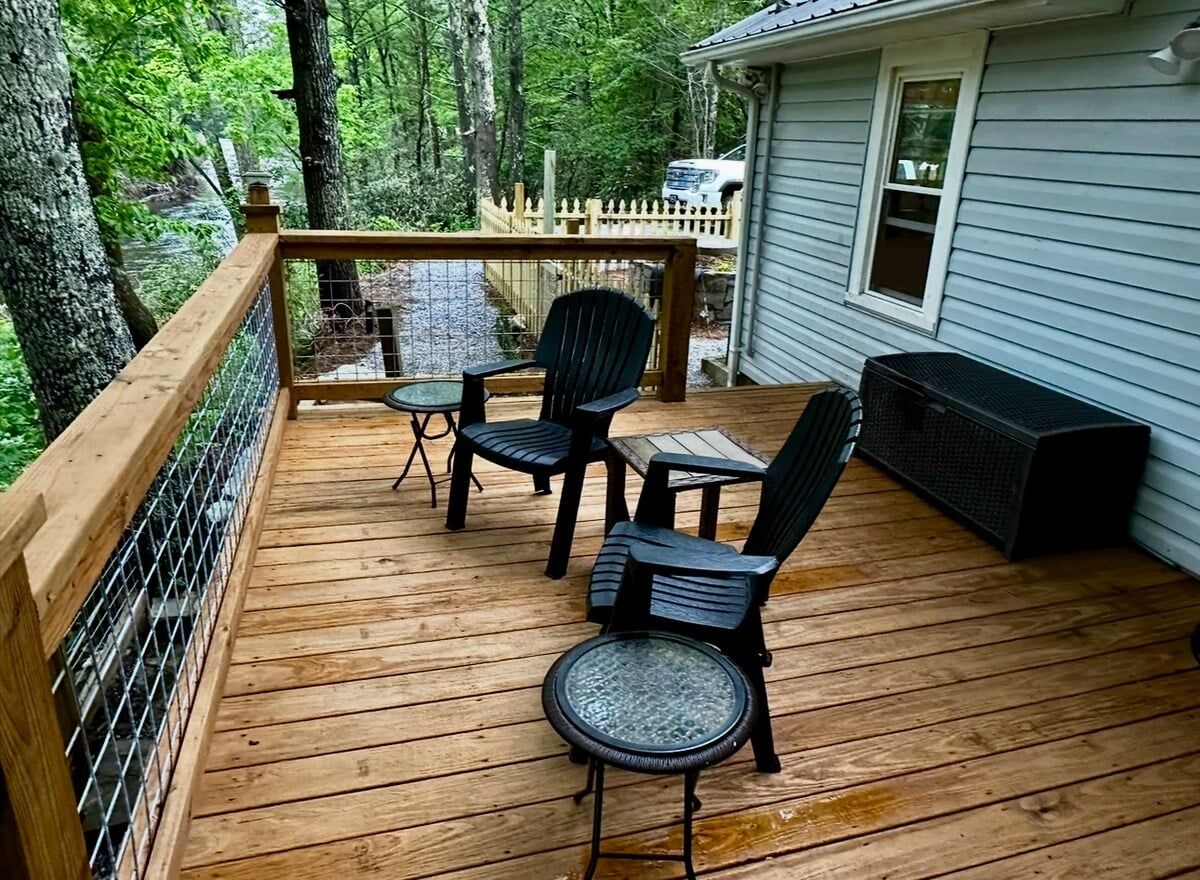 Una terraza de madera con mobiliario exterior, barandilla y una casa al fondo.