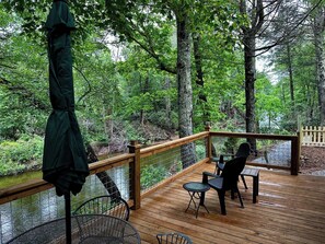 Een houten terras met een tafel en stoelen met uitzicht op een rivier, omringd door bomen.