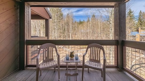 A wooden deck with two chairs and a table, overlooking a forested area.