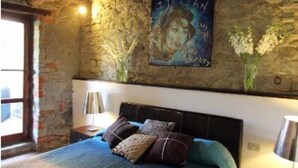 Une chambre avec un mur en pierre, un lit avec une literie bleue et une affiche accrochée au mur.
