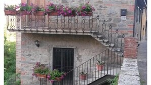 Un bâtiment en pierre avec une porte en bois, un balcon orné de jardinières et une petite fenêtre.