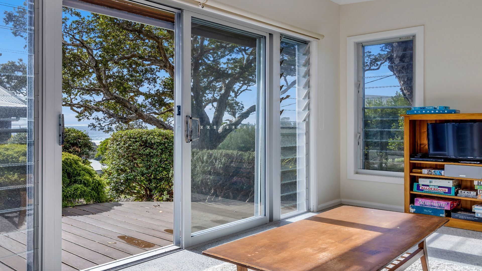A room with a wooden table, a bookshelf with games, and a sliding glass door leading to a deck.