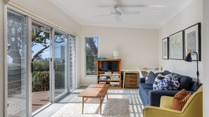 A modern living room with a sliding glass door, a ceiling fan, a wooden TV stand, a sofa, and a yellow armchair.