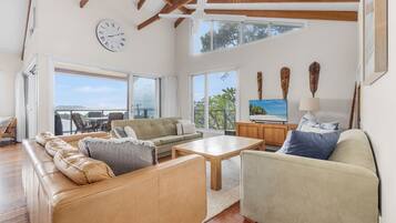 A spacious living area with a sofa, armchair, and coffee table, a television, and a balcony with a view.