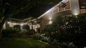 Une maison moderne dotée d’un éclairage extérieur soigné, d’un chemin de pierre menant à l’entrée et d’une végétation luxuriante tout autour.