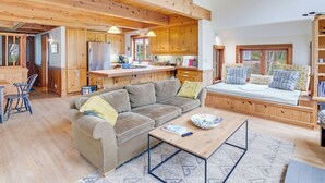 A spacious living area with a wooden ceiling, a sofa, a coffee table, and a kitchen in the background. - River to Breakers - River View (Yachats)