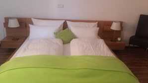 Una cama doble con ropa de cama blanca y verde, dos mesitas de noche con lámparas y un reloj verde sobre una de ellas.