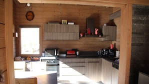 Cozinha compacta com paredes de madeira, área de refeições com mesa e cadeiras, e uma janela que traz luz natural.