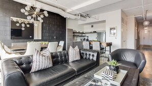 Ein modernes Wohnzimmer mit einer schwarzen Ledersofa, einem Couchtisch mit einem Schachspiel und einem Kronleuchter.
