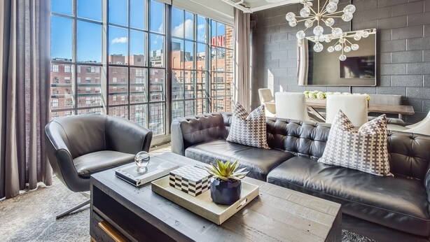 Ein modernes Wohnzimmer mit großem Fenster, Ledersofas, einem Couchtisch mit Pflanze und Blick auf die Stadt.