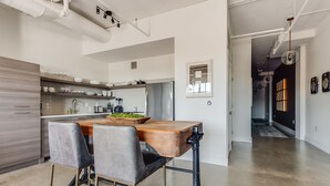 Eine moderne Küche mit Holztisch und Barhocker, einem Edelstahlkühlschrank und Blick in den Essbereich.