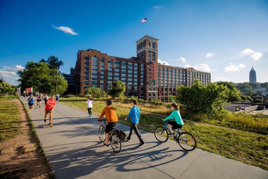 A large brick building with a tower and flag, surrounded by greenery and a pathway with people and cyclists.