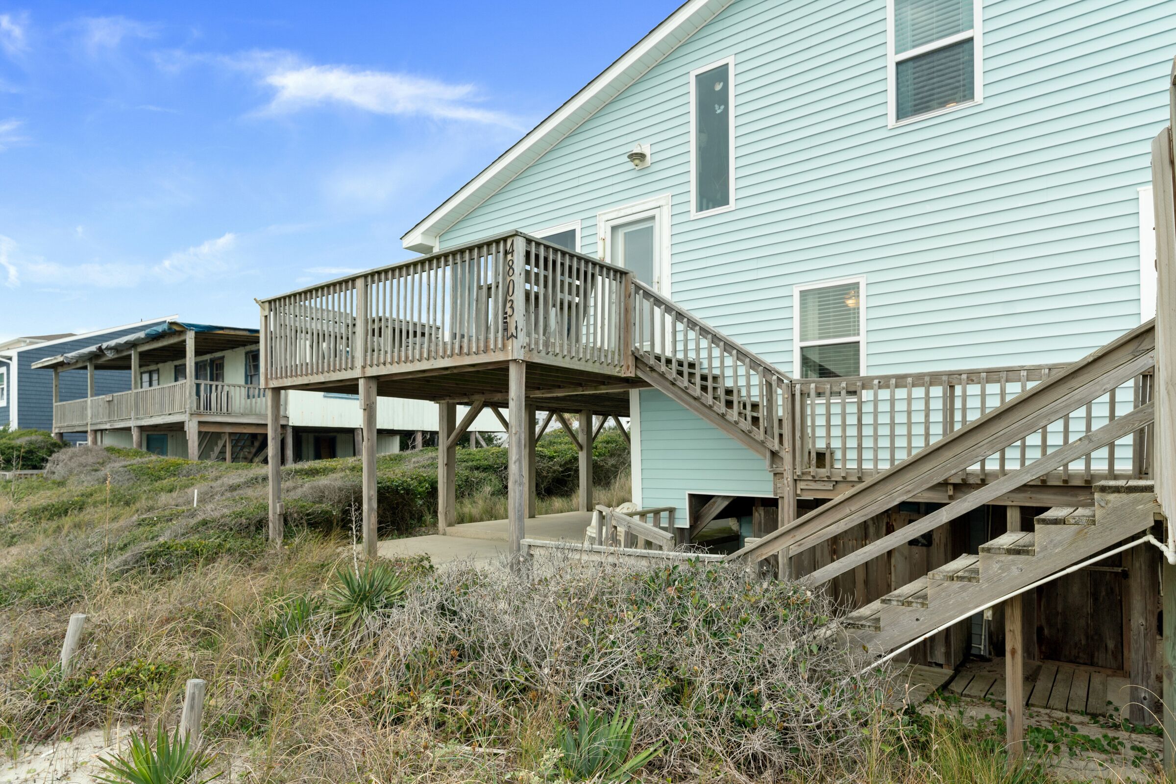 Een huis aan het strand met een houten terras en een trap naar een overdekte veranda.