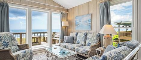 Un salón amplio con un gran ventanal con vistas al océano, amoblado con un sofá, sillones y una mesa de centro.