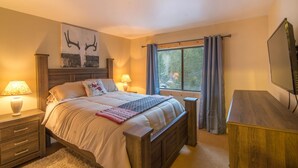 A bedroom with a bed, bedside tables, a desk, a window with curtains, and a TV.