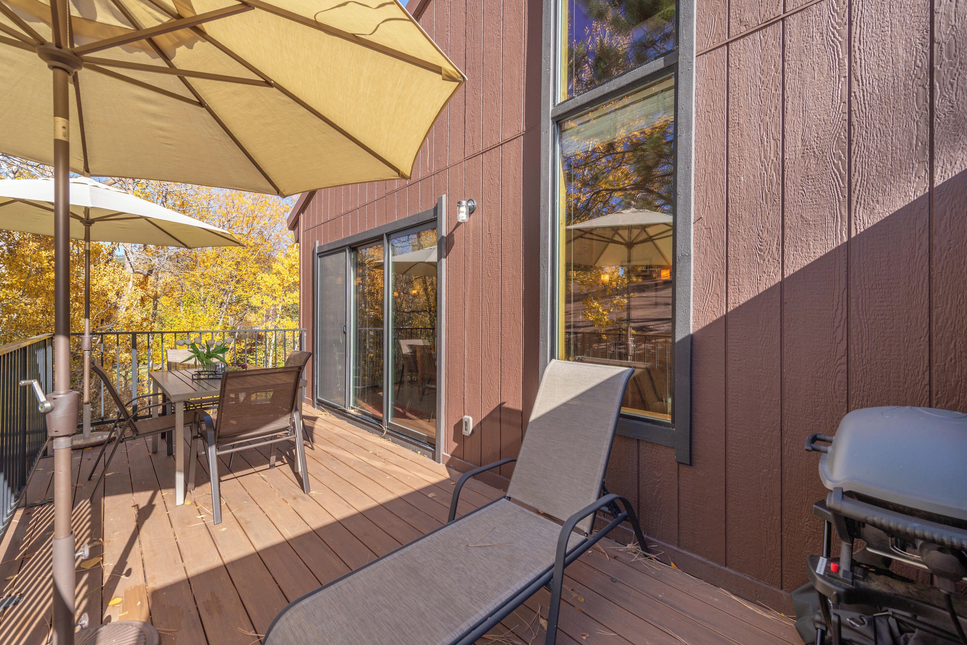 A wooden deck with a table and chairs, a grill, and a large umbrella.