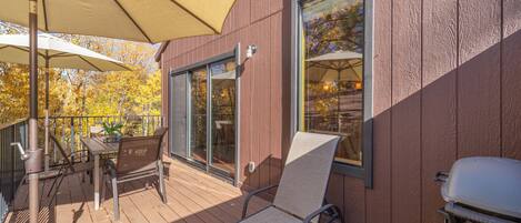 A wooden deck with a table and chairs, a grill, and a large umbrella.