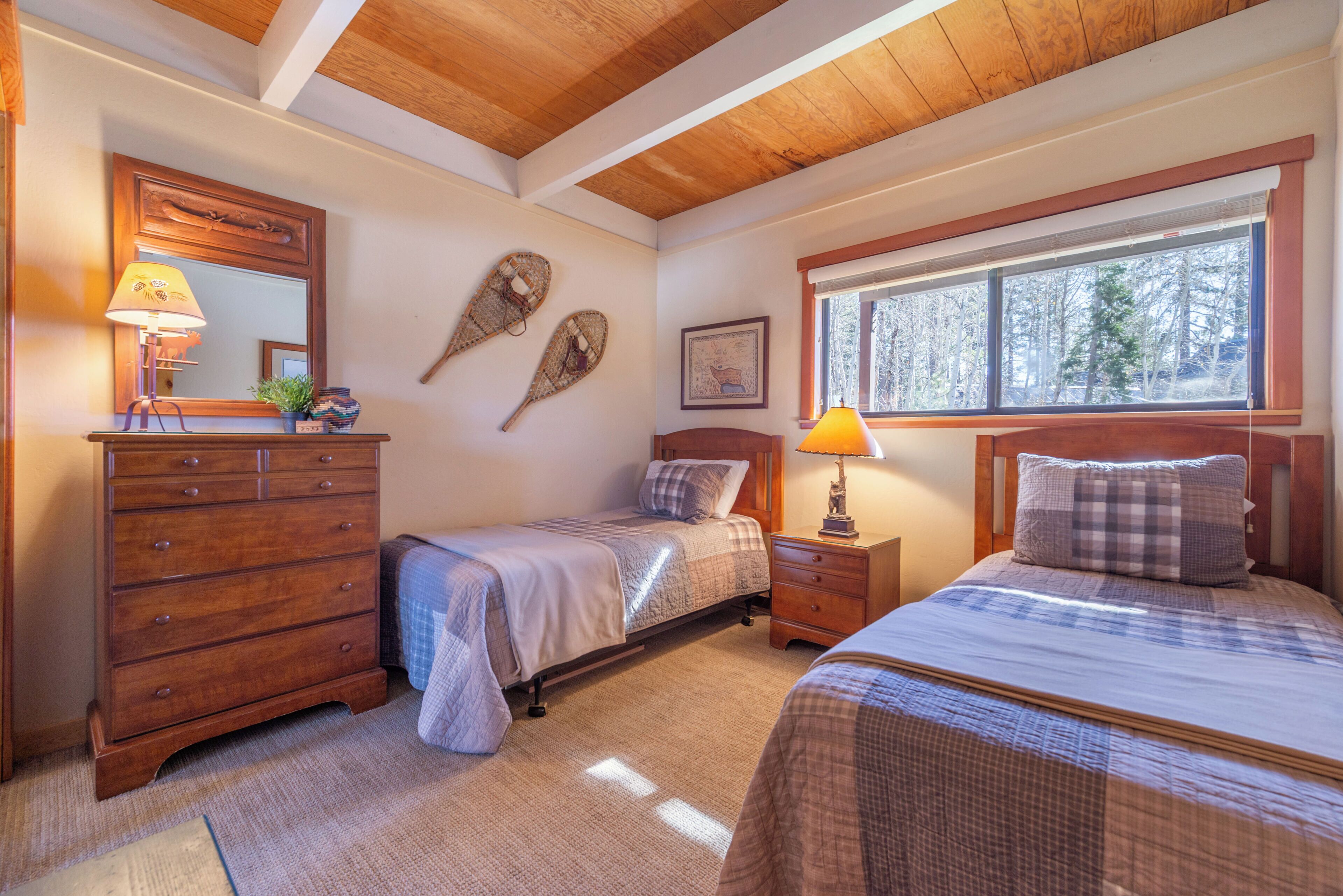 Une chambre avec deux lits, une commode, une fenêtre donnant sur des arbres et un miroir.