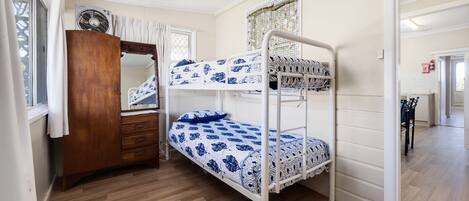 A bunk bed room with a wooden wardrobe, a mirror, and a patterned bedspread.