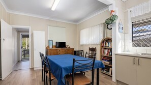 Une pièce comprenant une table à manger, des chaises, un téléviseur, une bibliothèque et une fenêtre donnant sur un beau paysage.