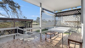 Eine überdachte Terrasse mit weißem Gitterzaun, einem Grill und einem Tisch mit Stühlen.