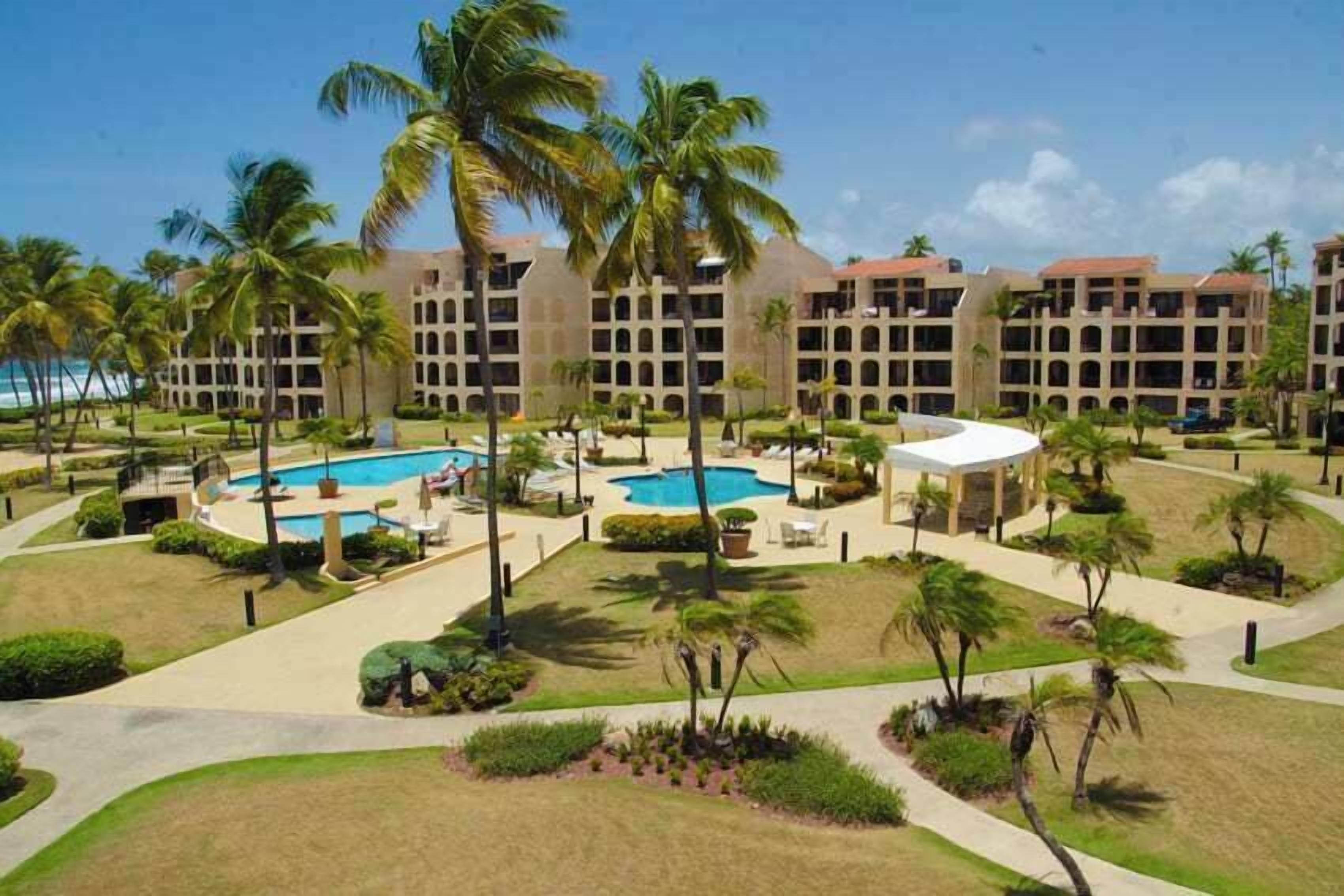 Ein Resort mit mehreren Swimmingpools, Palmen und einem großen Gebäude mit Balkonen.