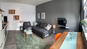 A modern living room with a grey sofa, a wooden dining table, and a TV. - Cozy 2 room apartment in Mainzer Bestlage (Oberstadt)
