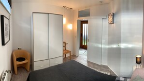 A modern bedroom with a bed, wardrobe, chair, and a small table with a lamp. - Cozy 2 room apartment in Mainzer Bestlage (Oberstadt)