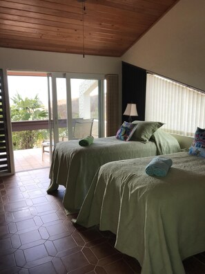 Une chambre avec deux lits, une chaise, une lampe et une vue sur l’extérieur.