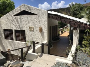 A building with a stone exterior, a sign reading "Cuvarey Hill," and a covered outdoor area with a patio and chairs. - Guavaberry Hill Villa - Amazing sunset views by National Park, No A/C (St. John)