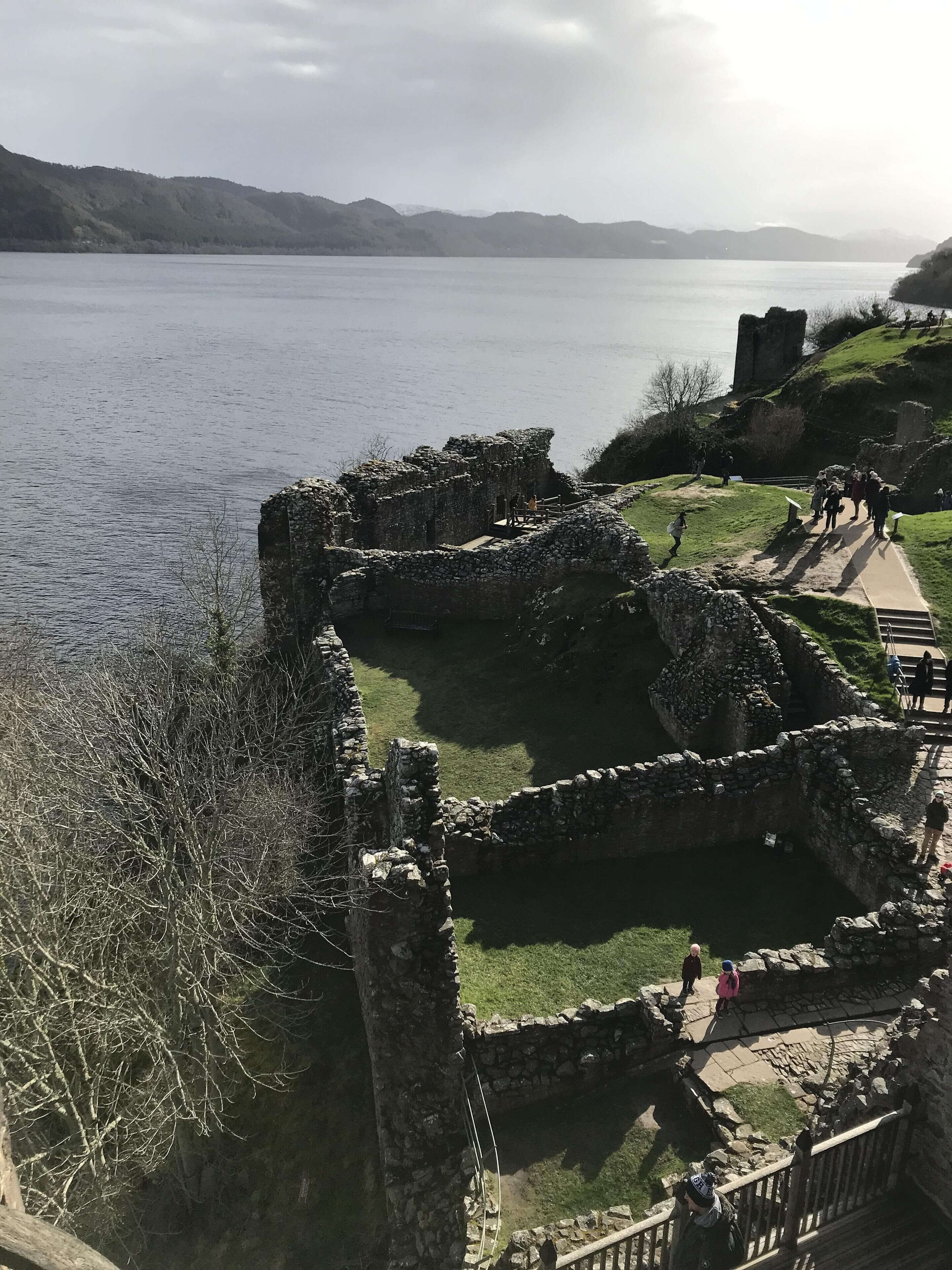 A historical site with stone ruins and a pathway leading to a grassy area by a lake.