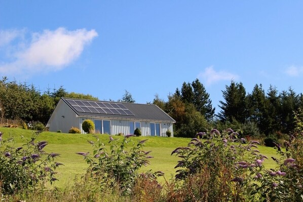 Un edificio de una sola planta con techo inclinado, paneles solares y un pequeño jardín delantero.