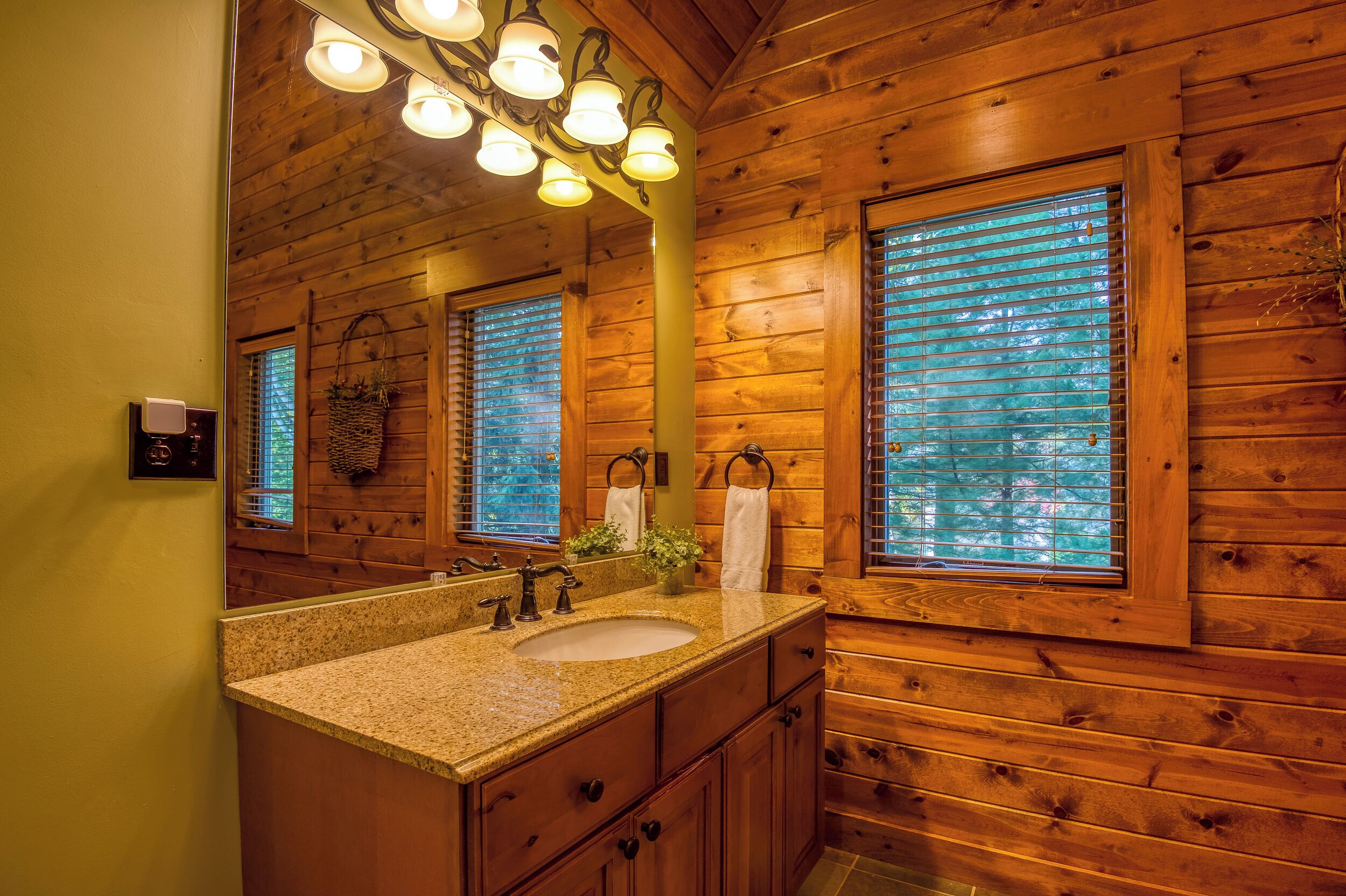 Baño de cabaña de madera con un espejo grande, dos lavamanos y paredes de madera.