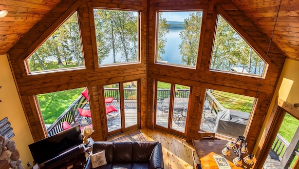 Une cabane dotée de grandes fenêtres donnant sur un lac et une forêt.
