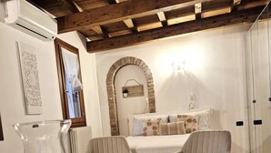 A cozy room with a wooden ceiling, a stone arch, a bed with patterned bedding, two armchairs, a table with a candle, and a radiator. - In the ancient Jewish ghetto (Ferrara)