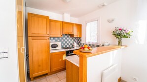 A compact kitchen with wooden cabinets, a microwave, a kettle, and a fruit bowl on the counter. - Chalet 4-6 pers. - Albaret-le-Comtal (Albaret-le-Comtal)