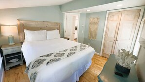 Un dormitorio con una cama grande, una mesita de noche, una lámpara, un colgador de macramé y una puerta.