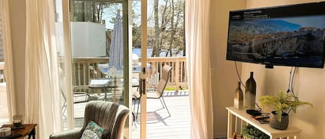 Ein gemütliches Wohnzimmer mit einem bequemen Sessel, einem an der Wand montierten Fernseher und Blick auf die Terrass.